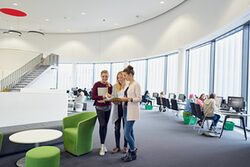 Drei Studentinnen blättern gemeinsam in einem Dokument.