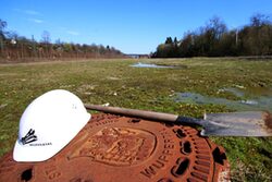 Bauhelm und Schaufel liegen auf einer schlammigen Wiese