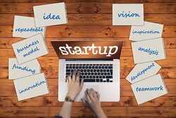 Auf einem Laptop-Monitor steht "Start-up". Darum verteilt liegen Notizen mit Themen, an die Gründerinnen und Gründer denken sollten.